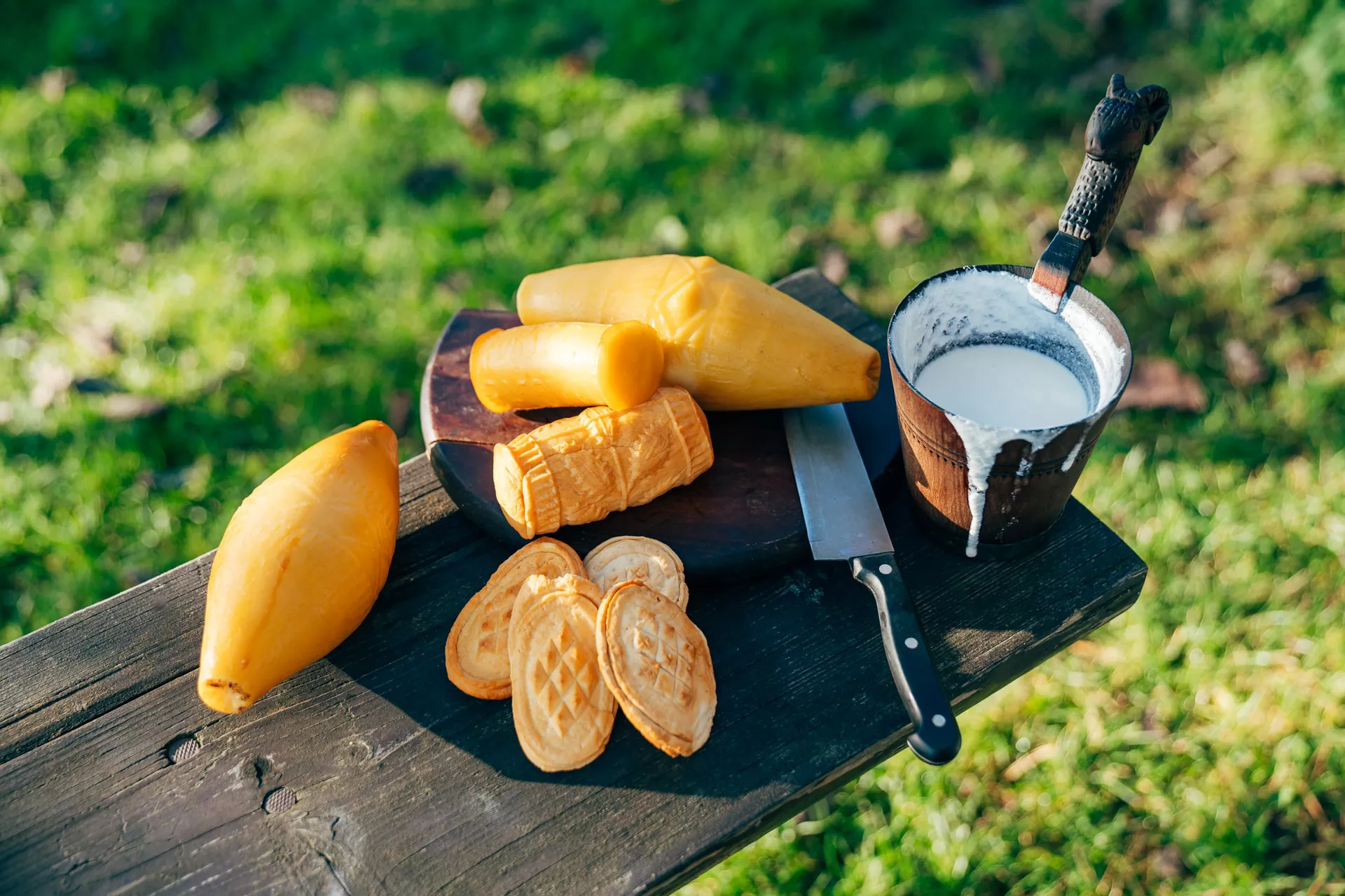 Oscypek, Gołka and other mountain cheeses of different shapes on a wooden bench, with a knife and a wooden pitcher with Żentyca sheep milk whey.