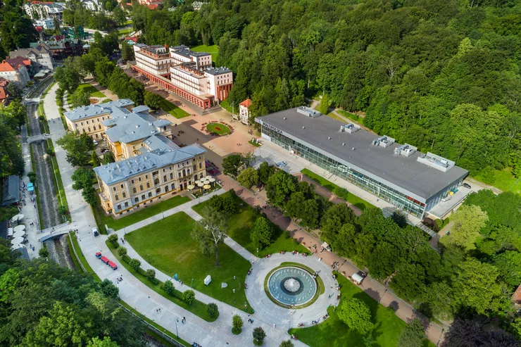 A bird’s eye view of the central part of Krynica SPA, with the neo-Renaissance mansion of the Old Spa House on the left, and the modernist Main Pumping Room and the sanatorium in the modernist New Spa House on the other side of the Central Promenade. At the top, the tree-clad slope on the right gives room to buildings that continue downwards along the Bulwary Dietla promenade over the Kryniczanka Stream along the left edge.