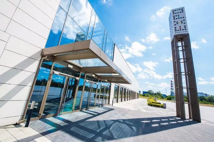 A view of the glazed entrance to a fair and congress venue fronted by an extensive empty car park with a tall post with the name of the venue.