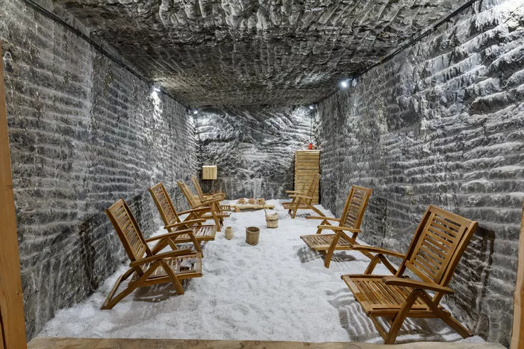 A view of a chamber roughly hewn in grey salt with comfortable wooden deckchairs arranged against the walls. Its floor is strewn with fine white salt.