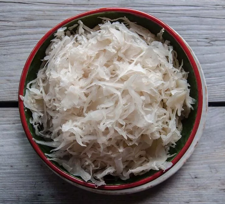 A view of a small bowl with thinly sliced cabbage standing on the planks of a wooden table.