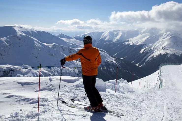 Blick auf einen Skifahrer, der am Anfang der Skipiste steht und die schöne Aussicht genießt. Rundherum sind die schneebedeckten Gipfel der Tatra zu sehen. Der Himmel ist blau mit weißen Wolkenfetzen.