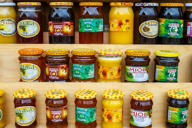 A view of three wooden shelves with properly labelled jars of natural honey.