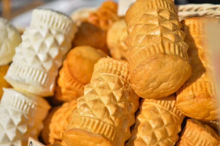 Several traditional smoked cheeses intricately decorated and fashioned into cylinders, some of them white and others dark orange, displayed in a wicker basket.