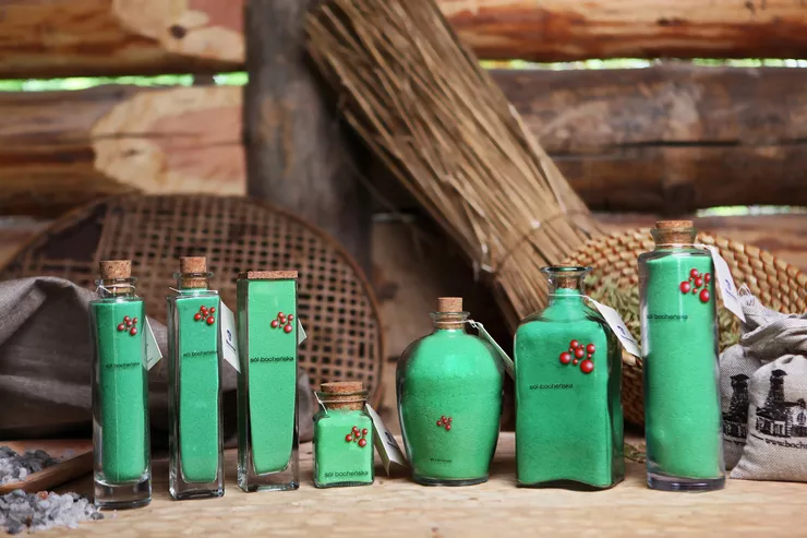 Glass containers with Bochnia bathing salts, all of them green and tightly corked, are displayed against a wooden fence.