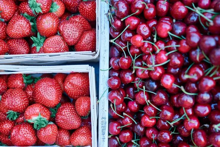 Beautiful ripe strawberries lie in two wooden baskets to the right of a larger basket with dark sweet cherries on the right.