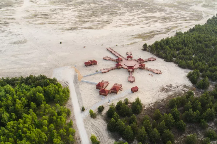 A bird’s eye view of the “Wind Rose” facilities for tourists, consisting of wooden platforms and shelters on the edge of a desert surrounded by trees.