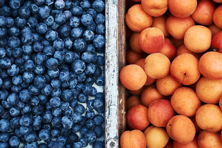 A view of ripe blueberries and apricots. The two types of fruit are separated with a wooden board painted white.