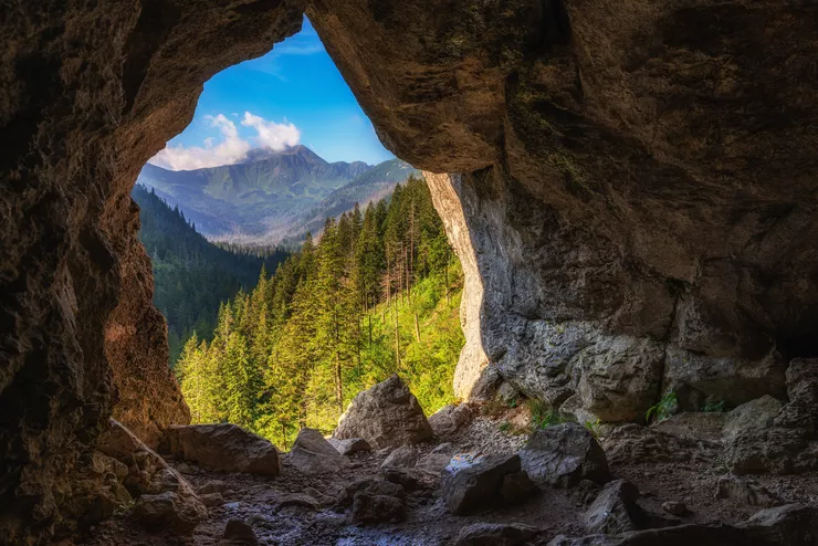 A breathtaking view of the Tatra peaks and sunlit wooded hills from the interior of a cave through the entrance to the cave known as Pawlikowski's Window.