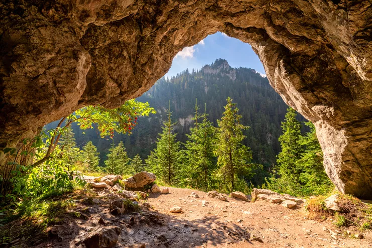 Der Blick aus dem Inneren der Höhle auf die Felsöffnung, durch die Sie die wunderschöne Landschaft der bewaldeten, sonnenbeschienenen Gipfel der Tatra sehen können.  Es ist ein wolkenloser Himmel.