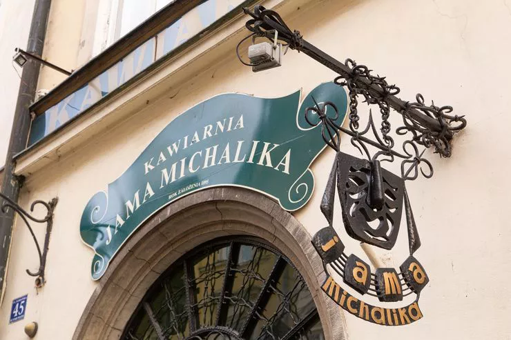 Ansicht der Hauswand mit dem grünen Schild mit der Aufschrift Café Jama Michalika. Unten sind ein Teil des Tores und das seitlich angebrachte Café-Schild zu sehen.