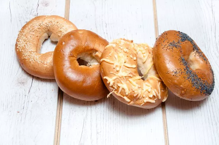 Four round bagels lying one on another, each sports a different topping. They all lie on a table built of white planks.