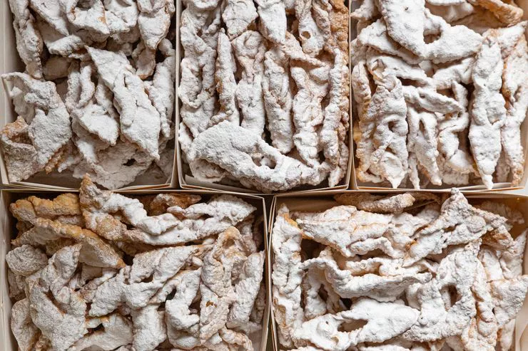 A peek into five boxes fully filled with elongated angel wings crispy pastries generously sprinkled with icing sugar.