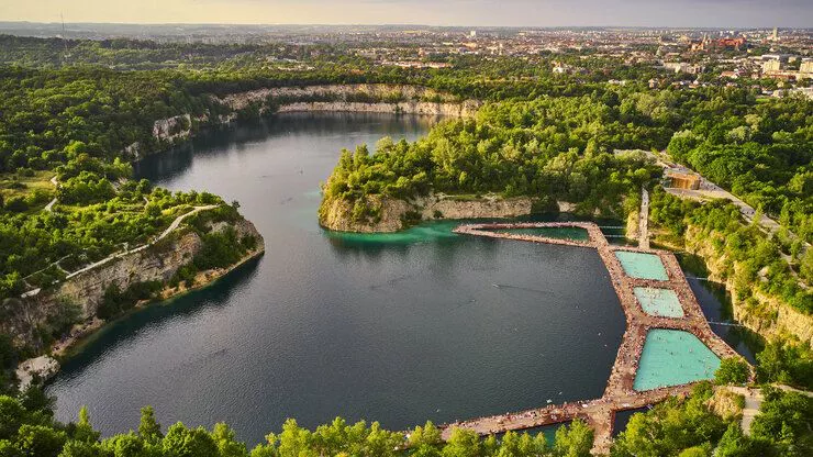 A bird-eye view of the lake in the abandoned quarry. The tops of its high limestone walls are crowned with words. Three recreational swimming pools connected with wooden gangways on the surface of the lake take the bottom right-hand corner.